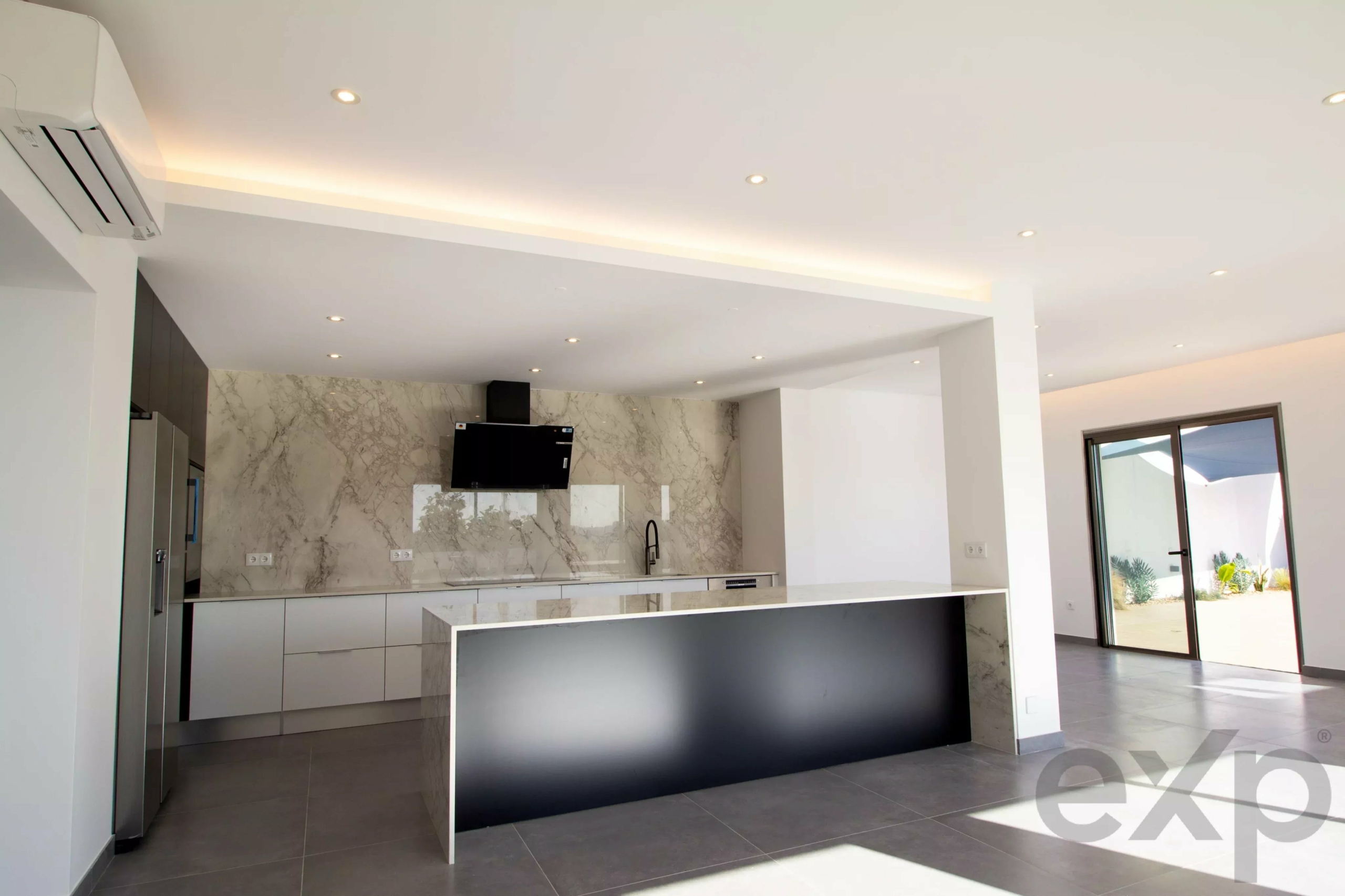 Modern kitchen with marble backsplash, grey cabinetry, and a black island under recessed ceiling lights.