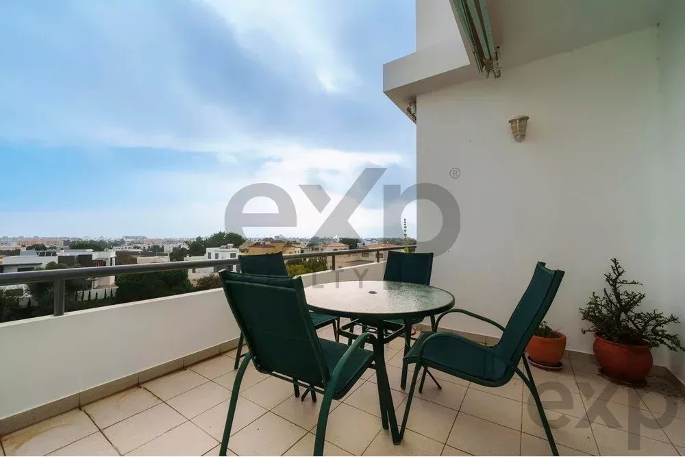 Balcony with a round glass table and four green chairs overlooking a cityscape.