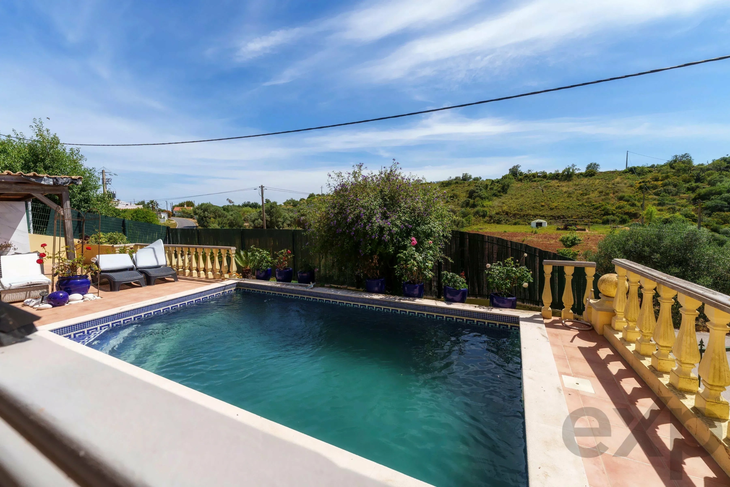 Poolside patio with a rectangular blue pool, terracotta deck, and yellow balustrade under a clear blue sky.
