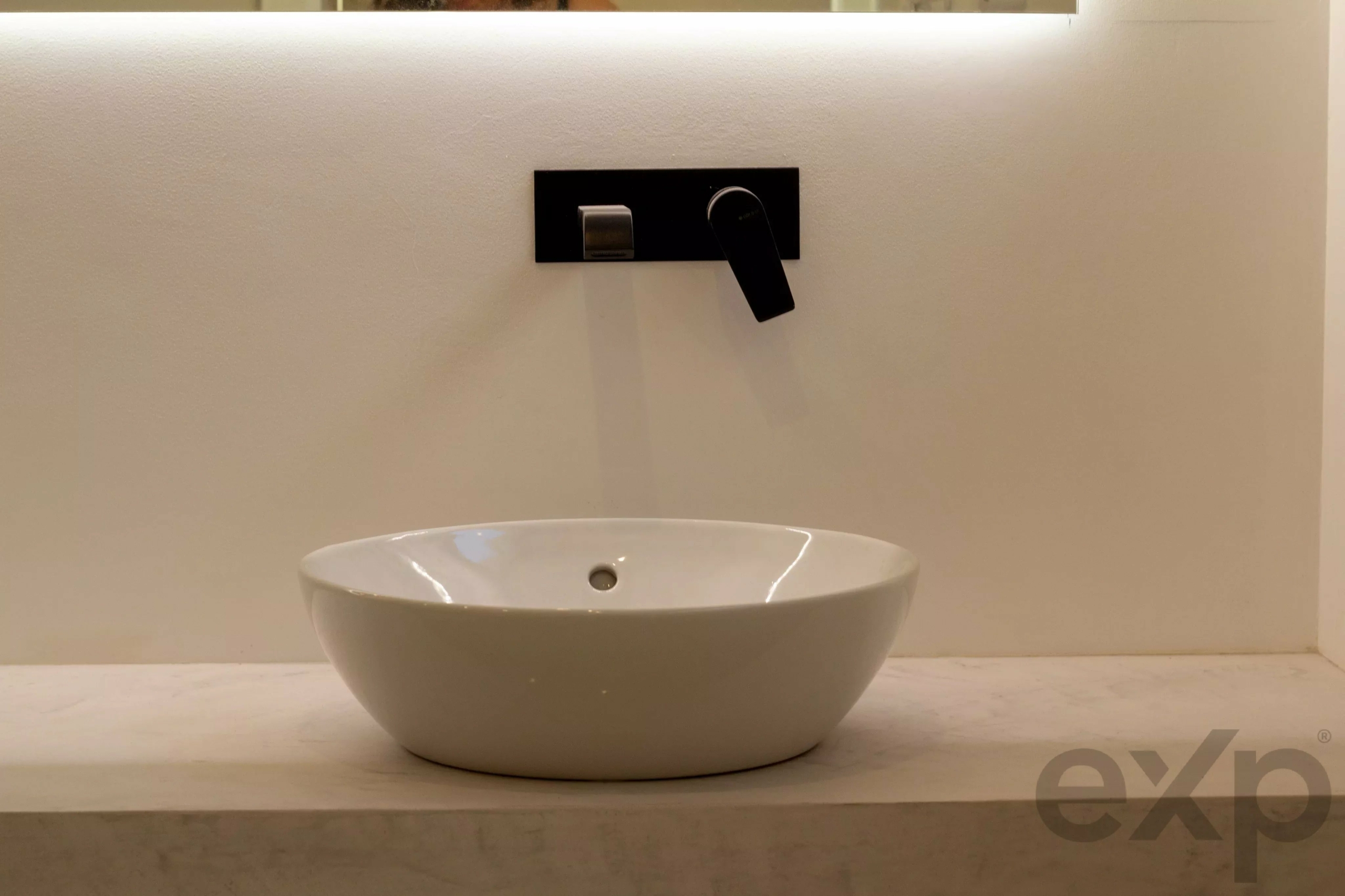 Modern bathroom scene: white round vessel sink on marble counter with a black wall-mounted faucet above it.