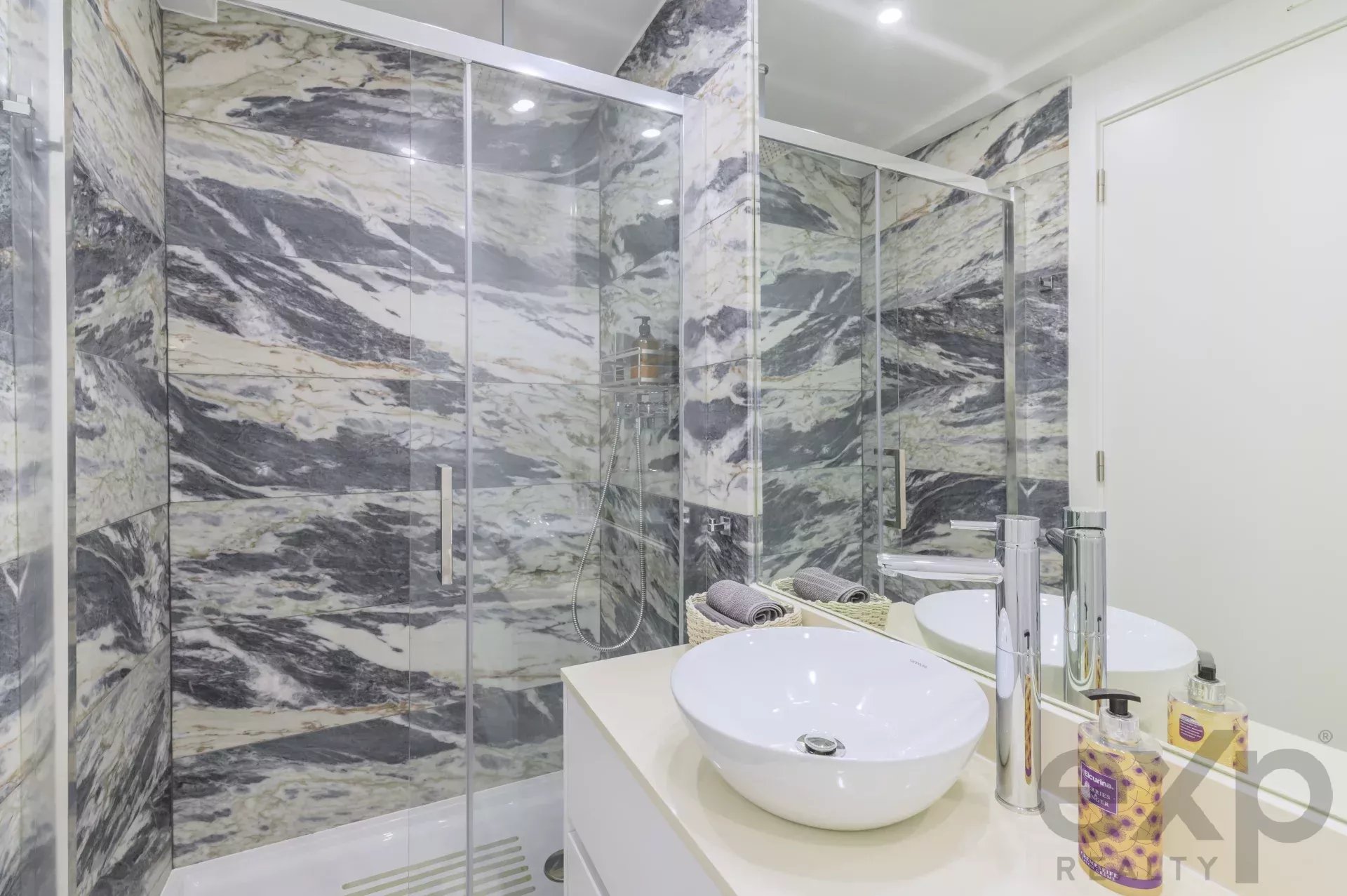 Modern bathroom featuring a marble-tiled shower area with a glass enclosure and a white vessel sink on a light countertop.