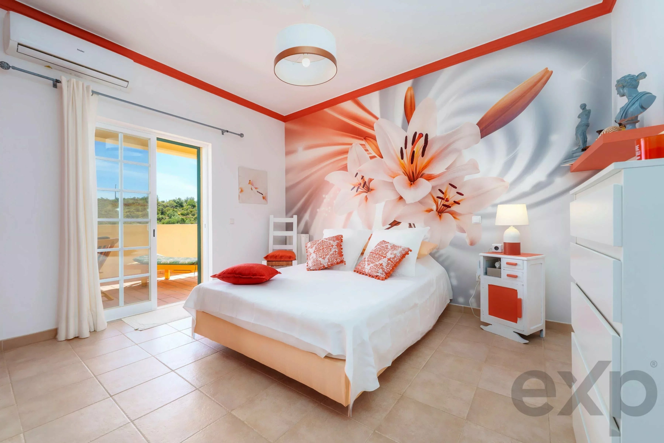 Bright bedroom with a large pink lily mural on the wall, white furniture, and orange accents surrounding the room.