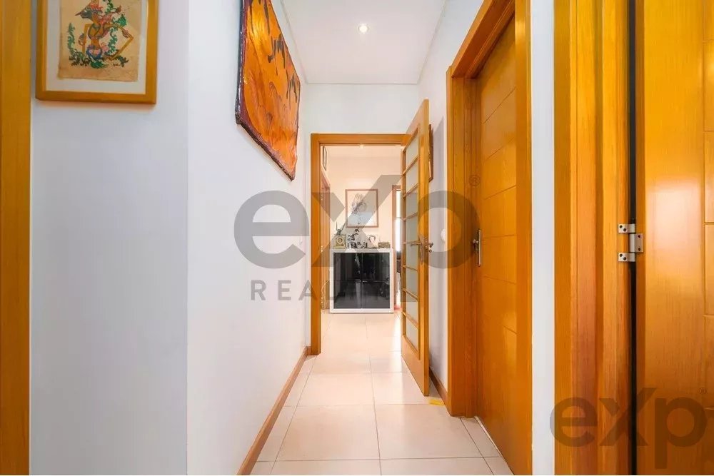 Bright hallway with white walls, glossy tile floor, and wooden doors on both sides, with framed art above the left wall.