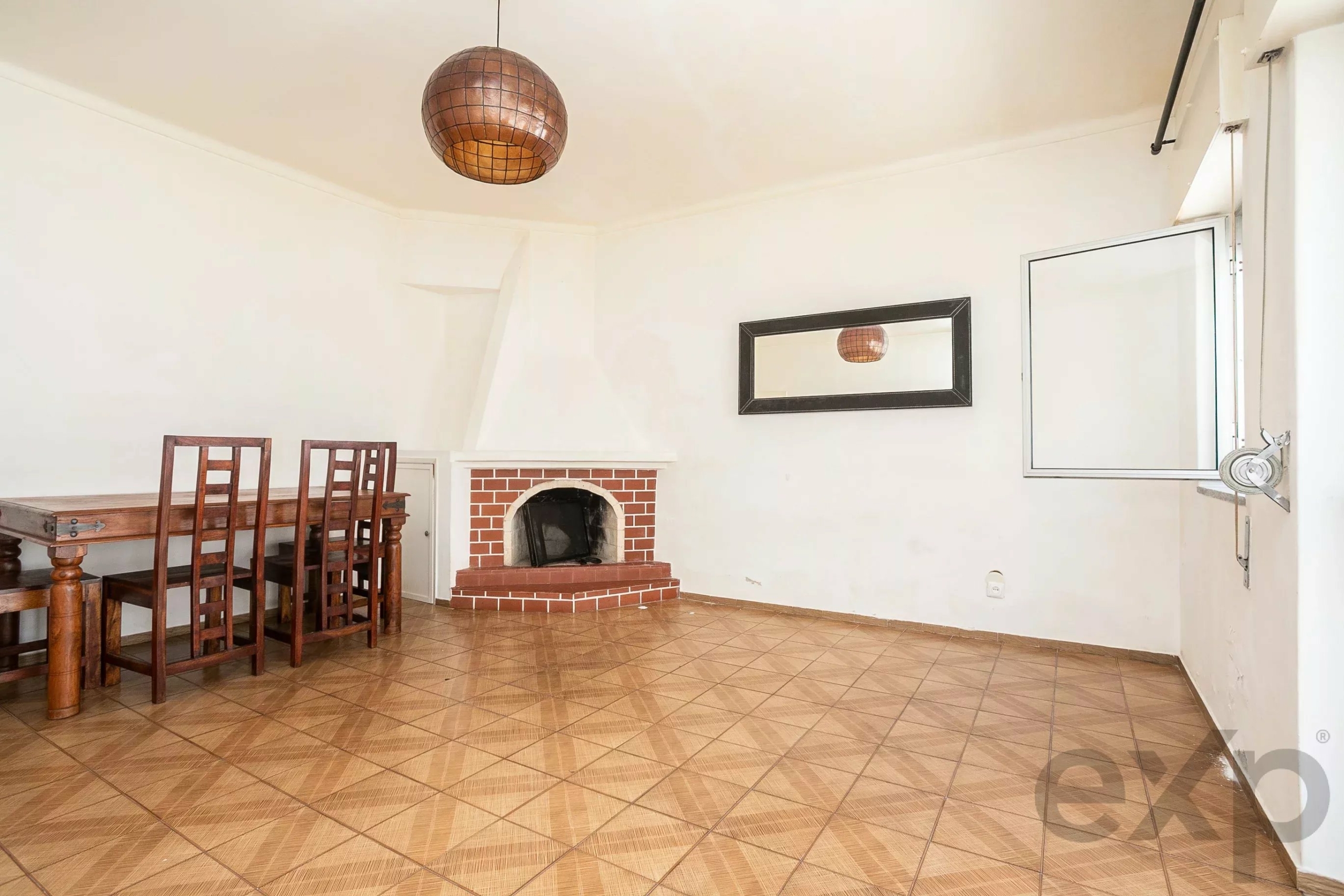 Dining room interior with a wooden dining table and chairs, brick fireplace, and a large wall mirror on white walls.