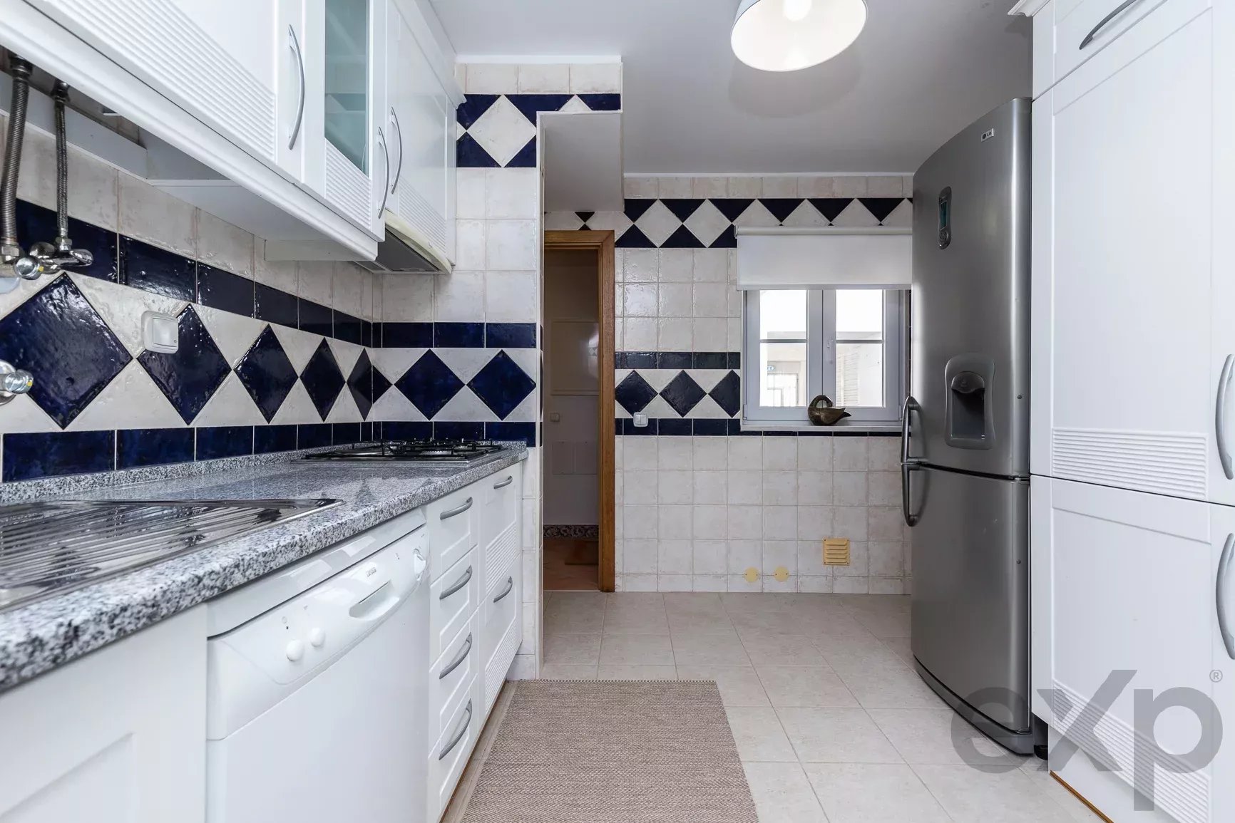 Kitchen with white cabinets, granite counter, blue-and-white diamond tile backsplash, and a large stainless steel refrigerator on the right.
