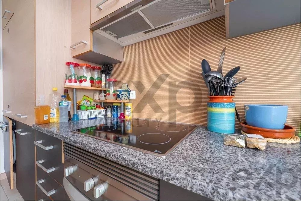 Modern kitchen countertop with an electric stovetop, utensils in a colorful jar, and organized spice jars on the left shelf