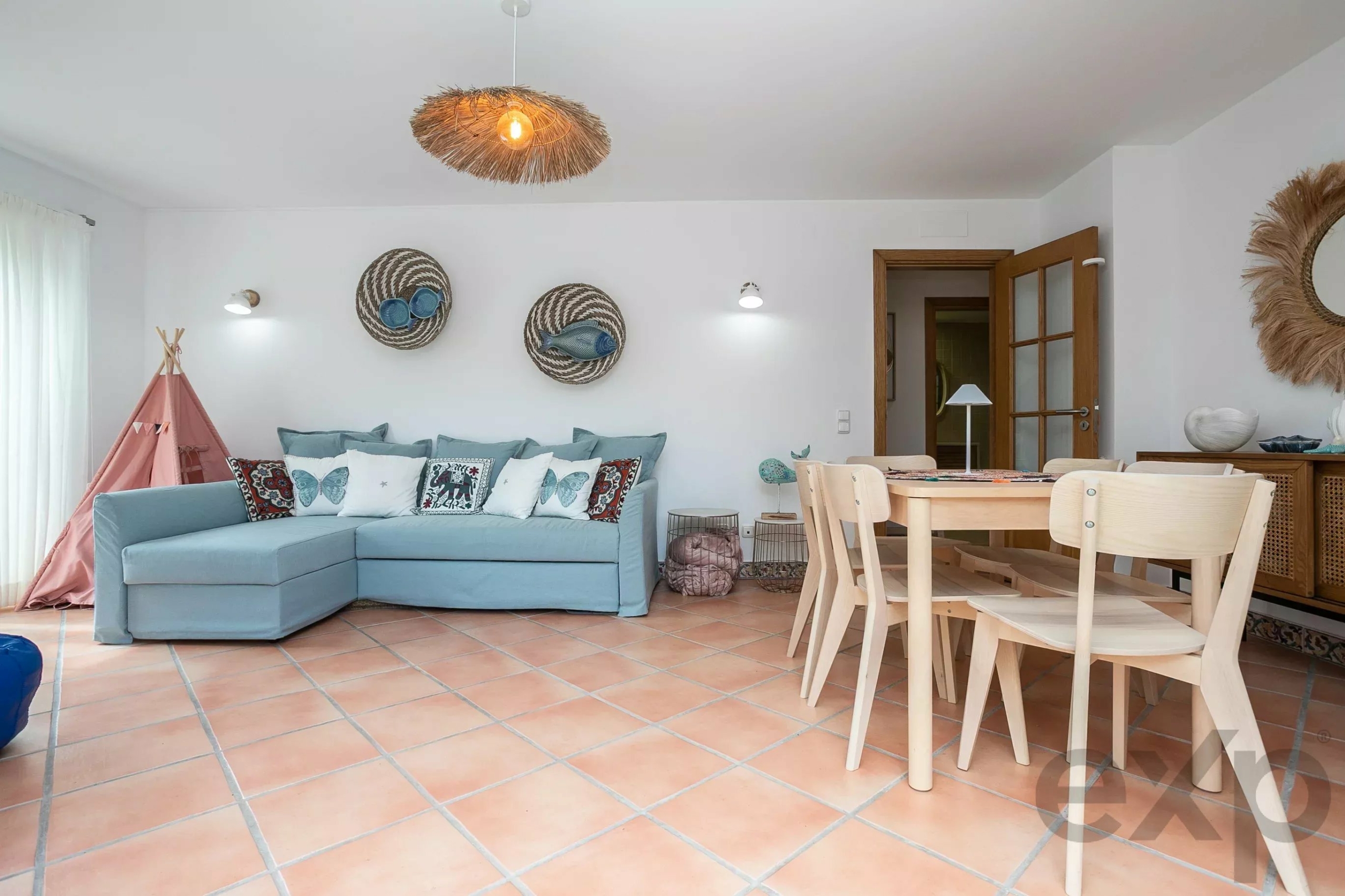 Coastal living room with a light blue sectional sofa, decorative cushions, and round woven wall baskets under a pendant light.