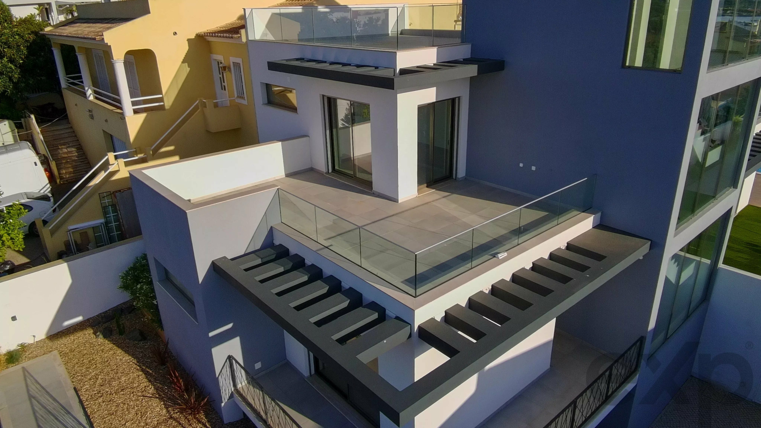 Aerial view of a modern multi‑story building with white, blue, and yellow walls, glass railings, and rooftop terraces.