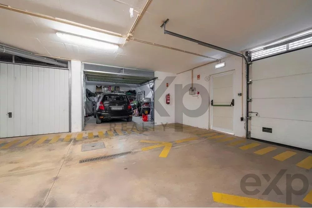 Indoor parking/garage space with a black car parked in an open service bay, cluttered with shelves and tools in the back.