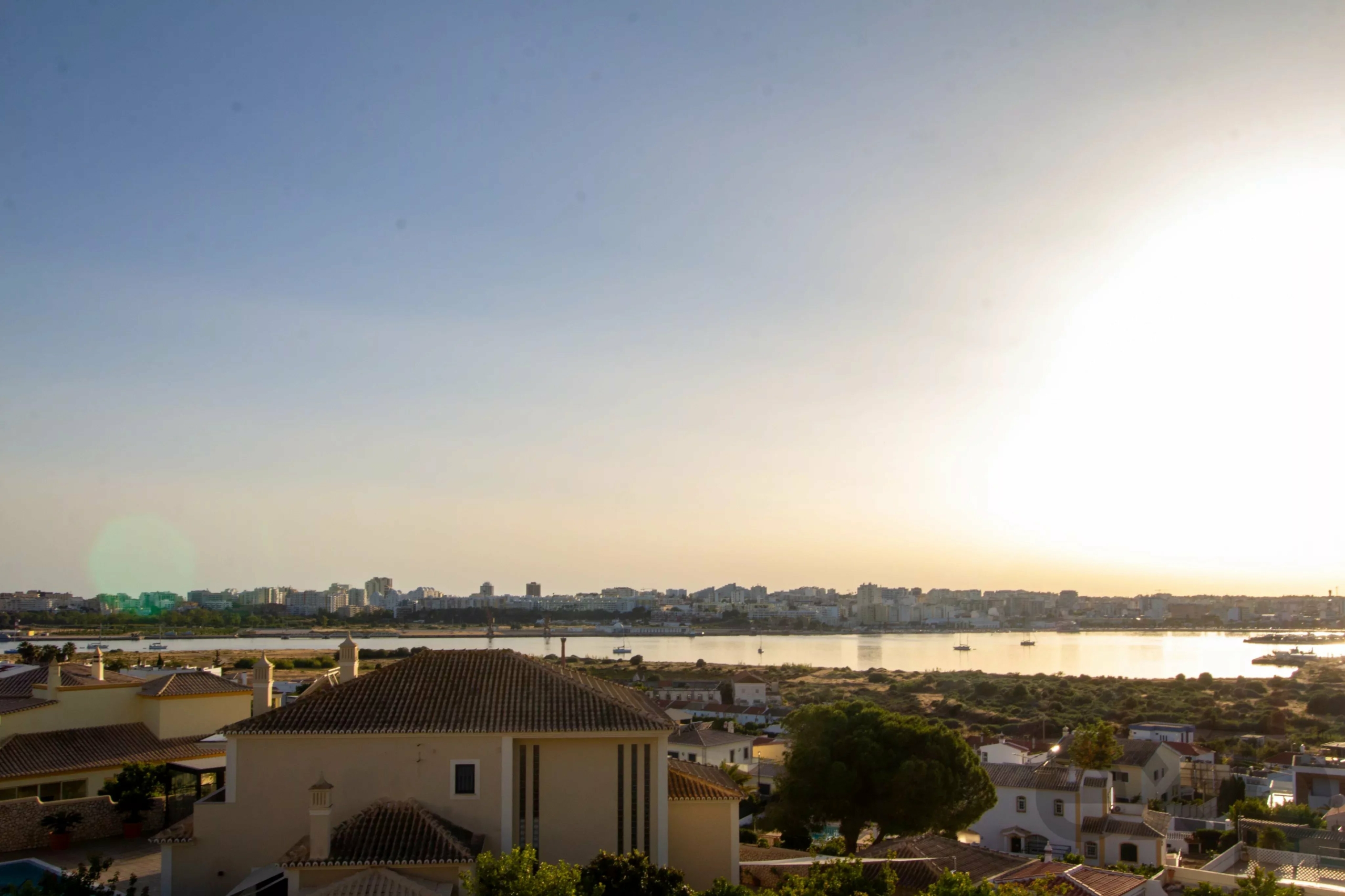 Sunset over a coastal city with low houses in the foreground and a river reflecting the light