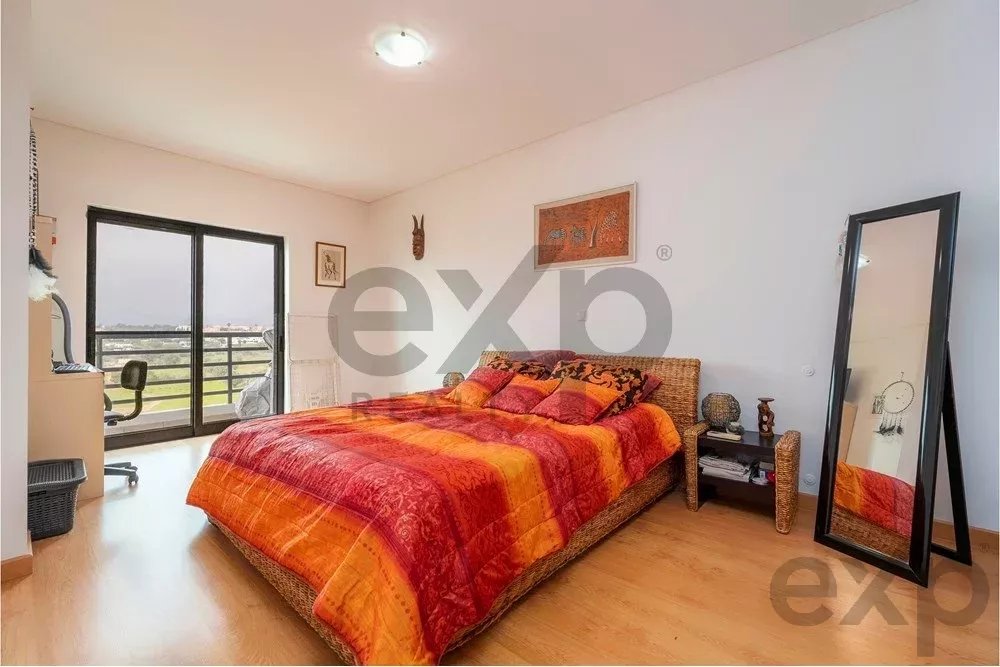 Bedroom with a large wicker bed and bright orange-red bedding, flanked by nightstands and a full‑length mirror; sliding balcony doors in the background.