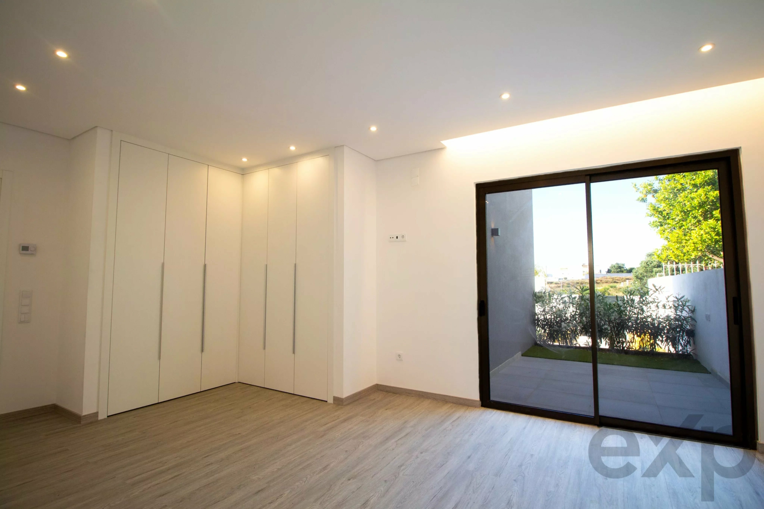 Bright modern room with tall white built-in cabinets along left wall and a large glass sliding door opening to an outdoor patio garden.