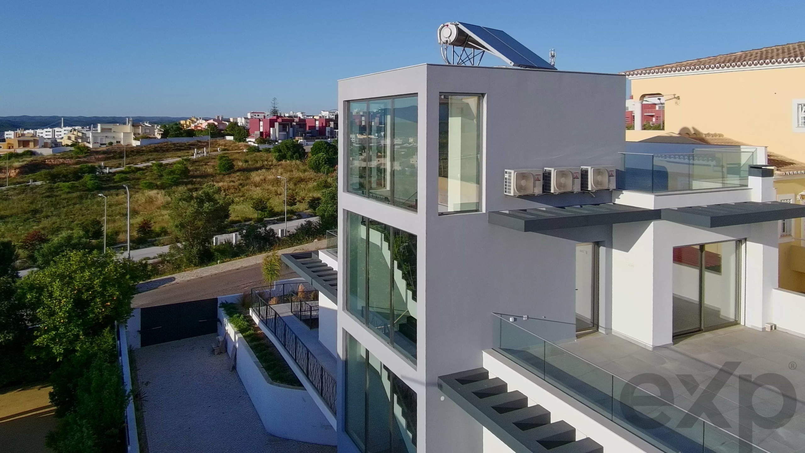 Modern white apartment building with large glass windows and a rooftop solar water heater under a clear blue sky.