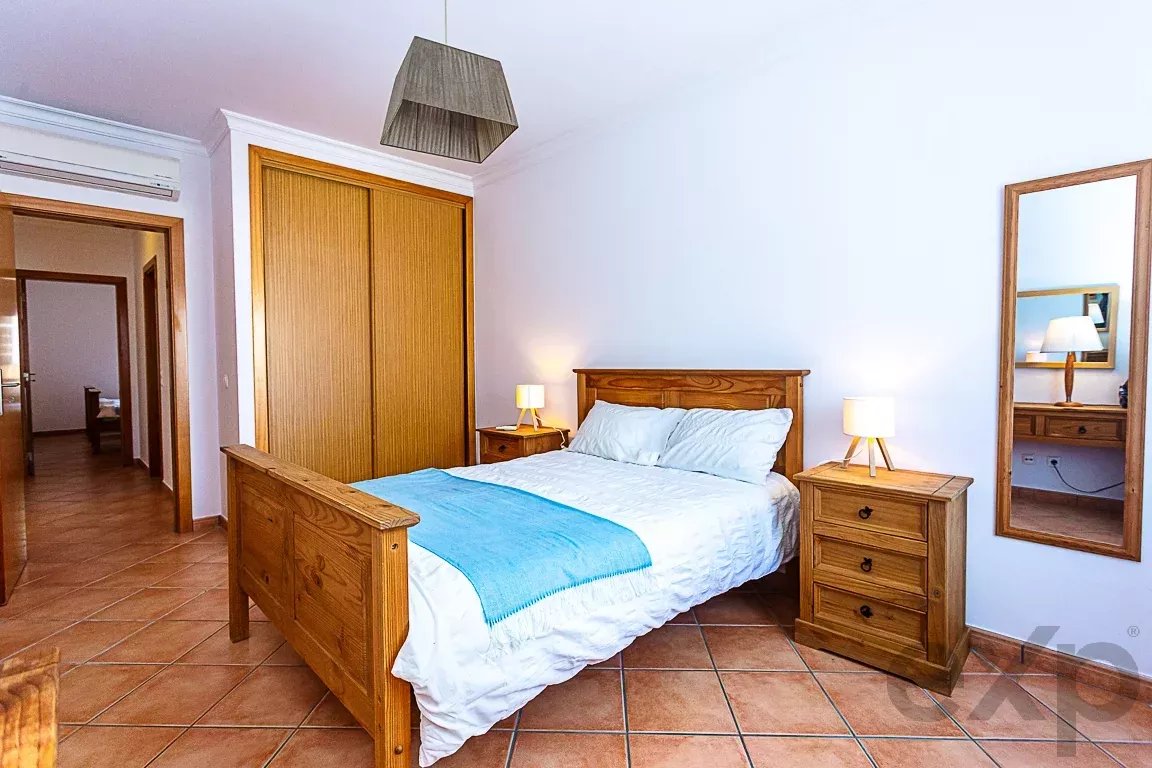 Wooden double bed with light blue throw, two matching nightstands and lamps in a bright bedroom.