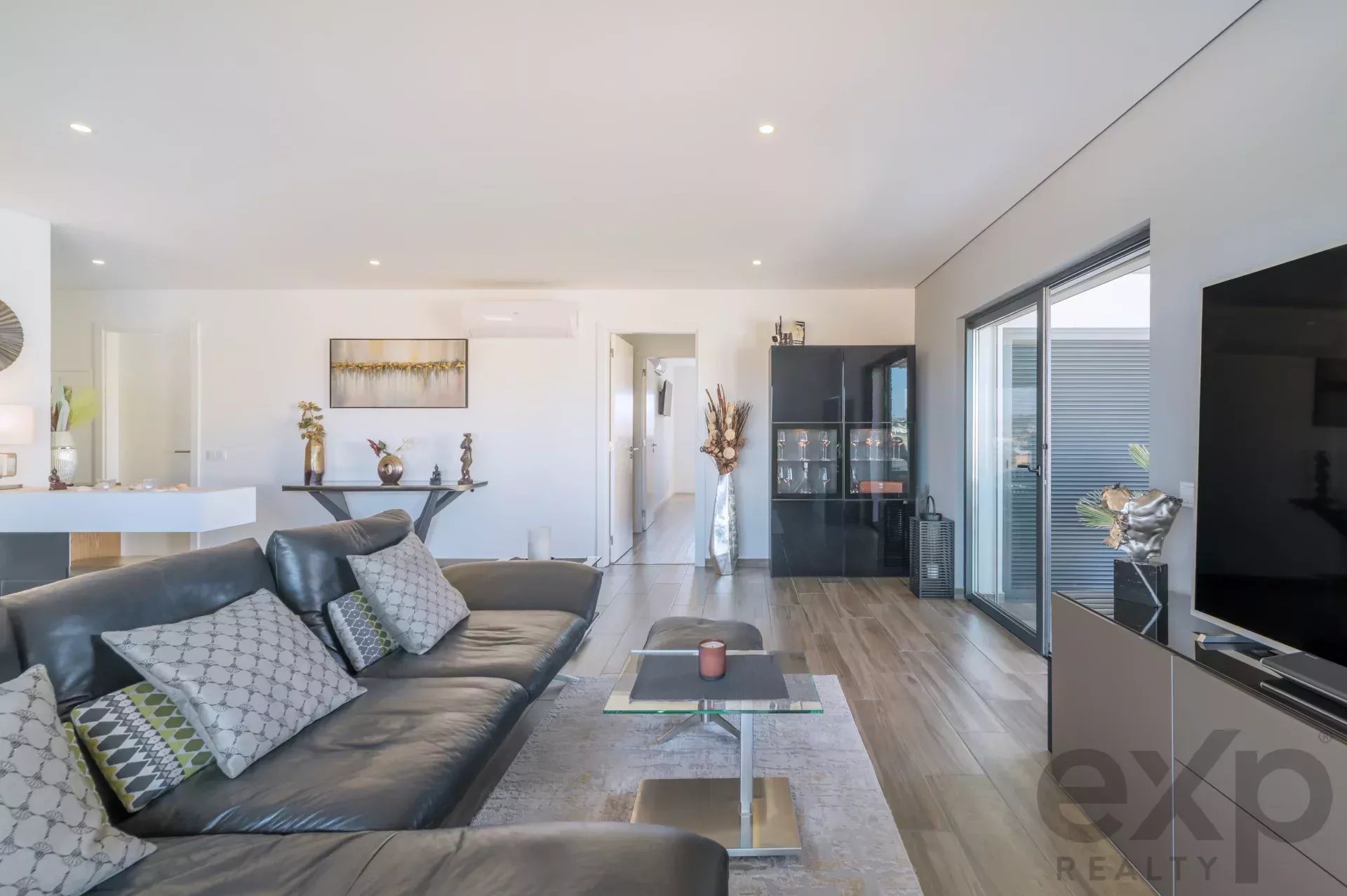 Open-plan living room with a gray sectional sofa, glass coffee table, and large sliding glass doors to an outdoor area.