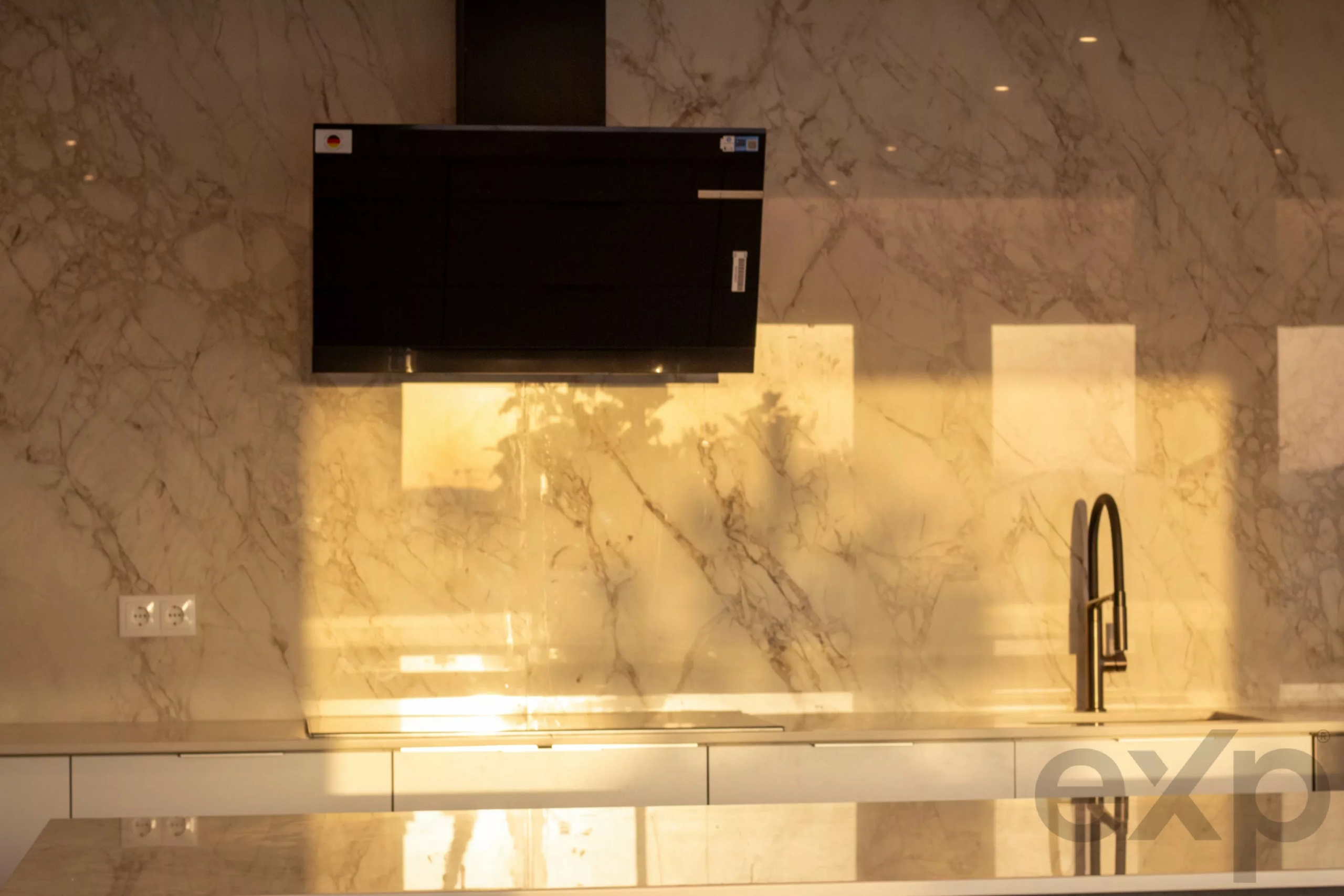 Modern kitchen with a black range hood, marble backsplash, and a tall faucet on the right.