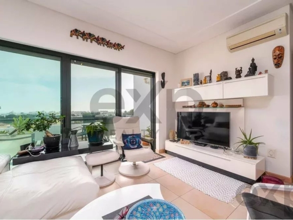 Bright living room with large glass doors to a balcony, white sofa, and a wall-mounted TV on a minimalist white entertainment unit with plants nearby.
