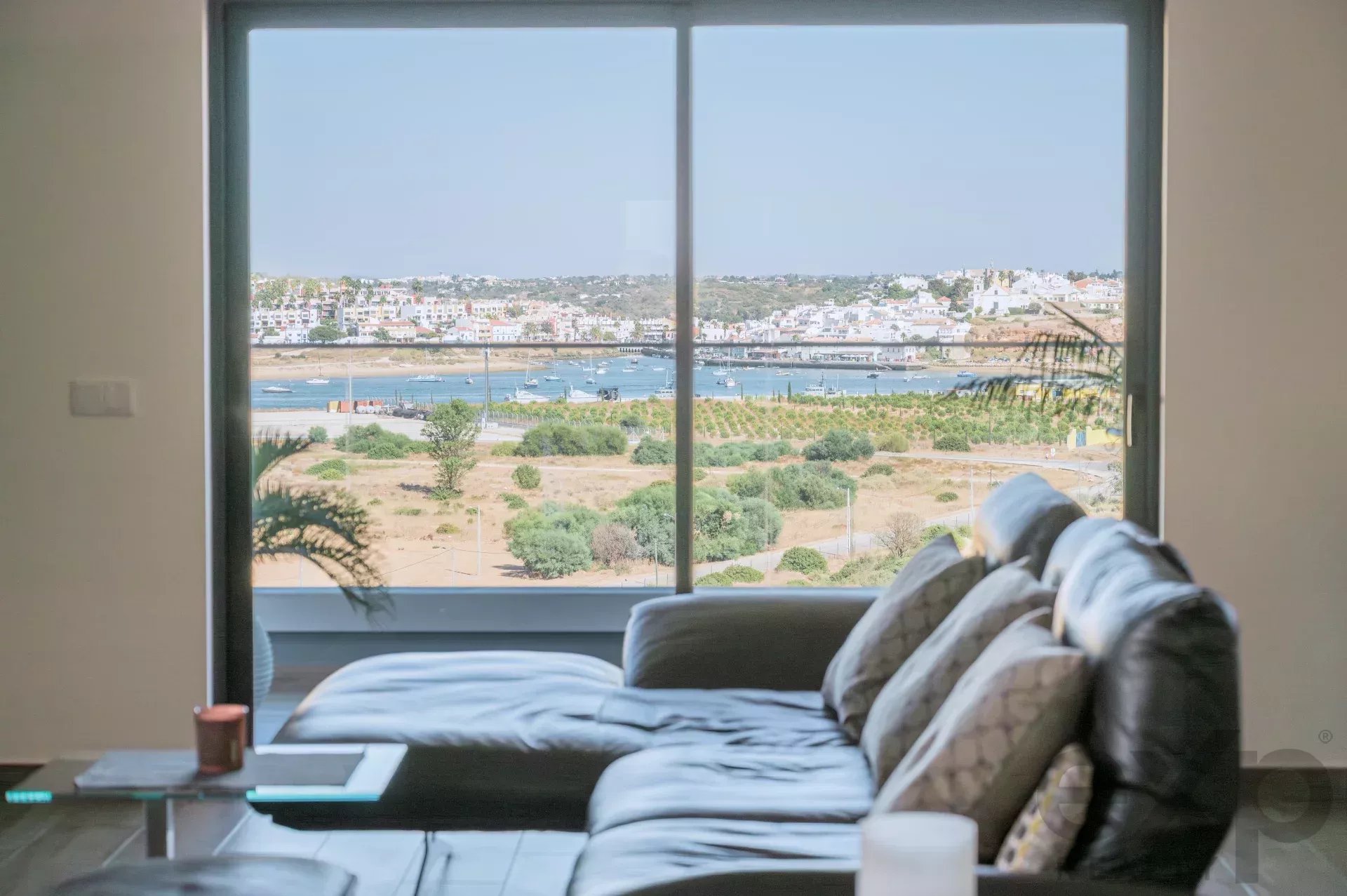 Living room with a large window showing a coastal harbor and boats; sofa with patterned cushions in the foreground.