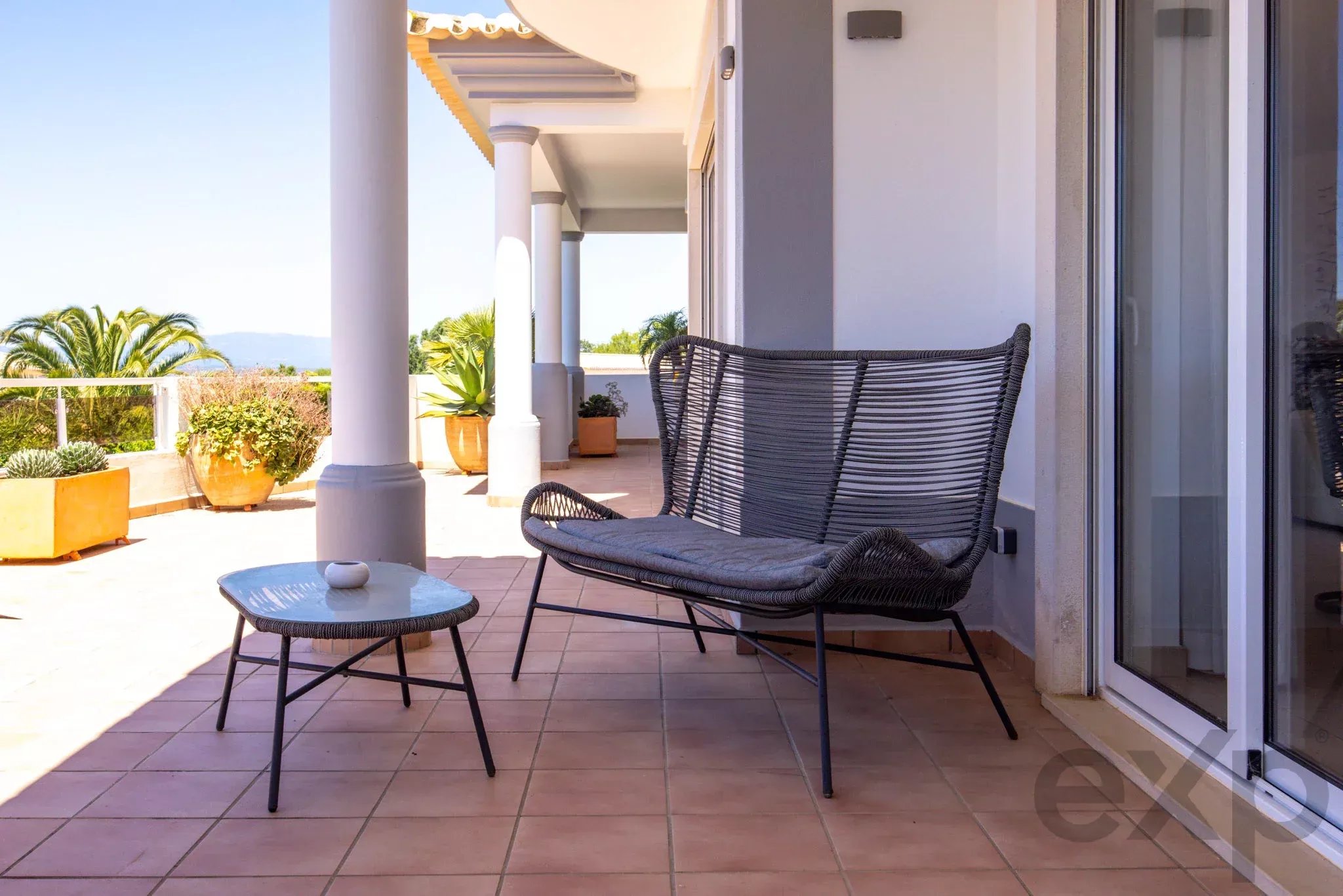 Outdoor balcony with two black wicker chairs and a small glass table on a sunny terrace.
