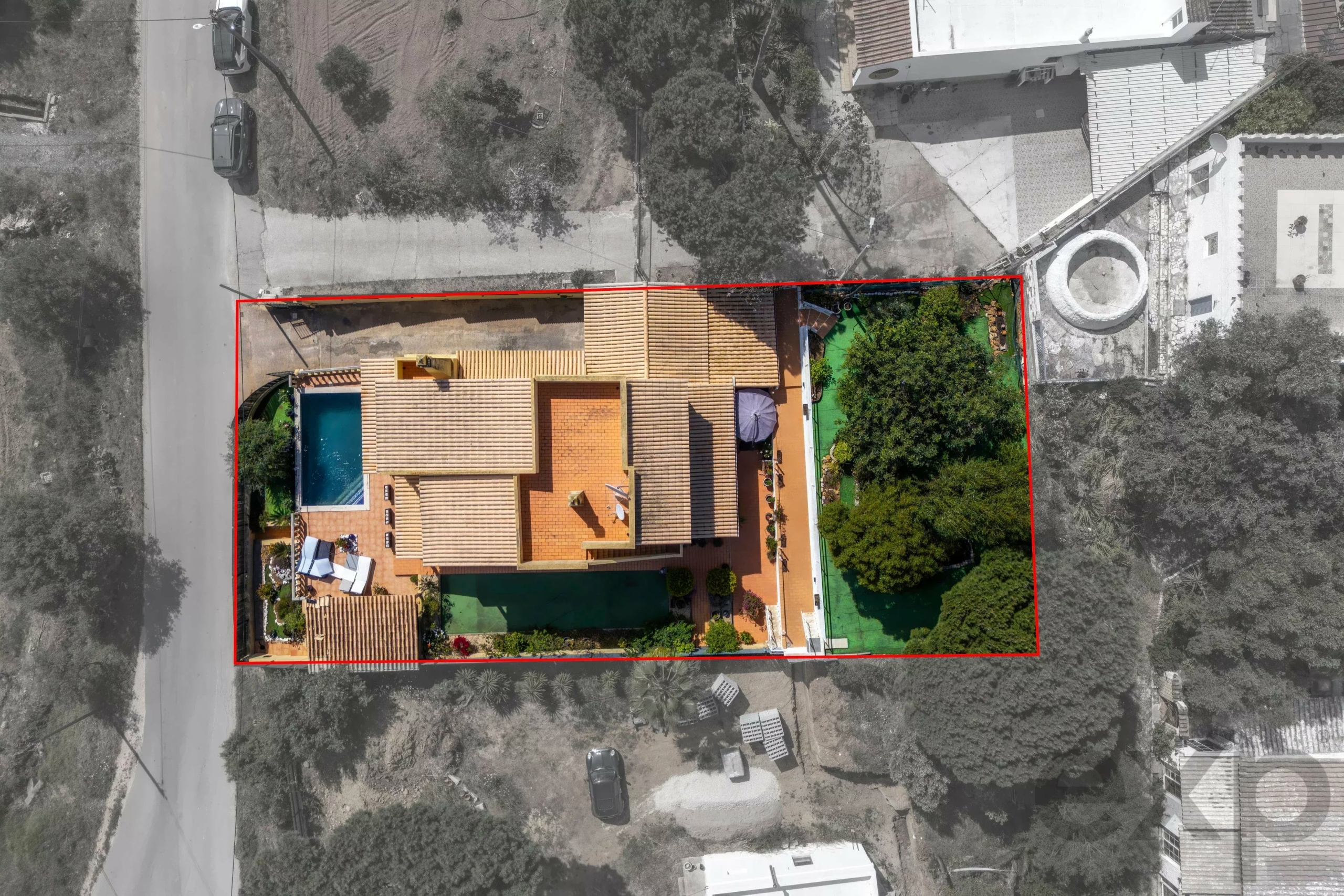 Aerial view of a house with orange tile roof inside a red-outlined lot, showing a pool, green yard, and surrounding neighborhood roads.",
