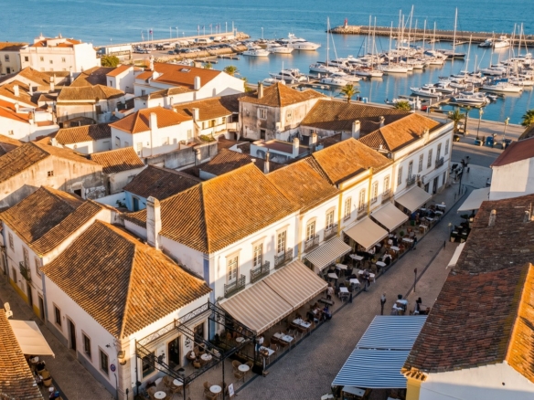 Aerial view at golden hour over an Algarve old town, terracotta rooftops, waterfront cafes and a marina full of yachts