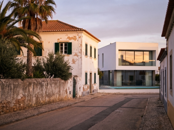 An older whitewashed Portuguese villa with green shutters next to a modern white flat-roofed new build with a pool on a quiet street in Lagos, Algarve