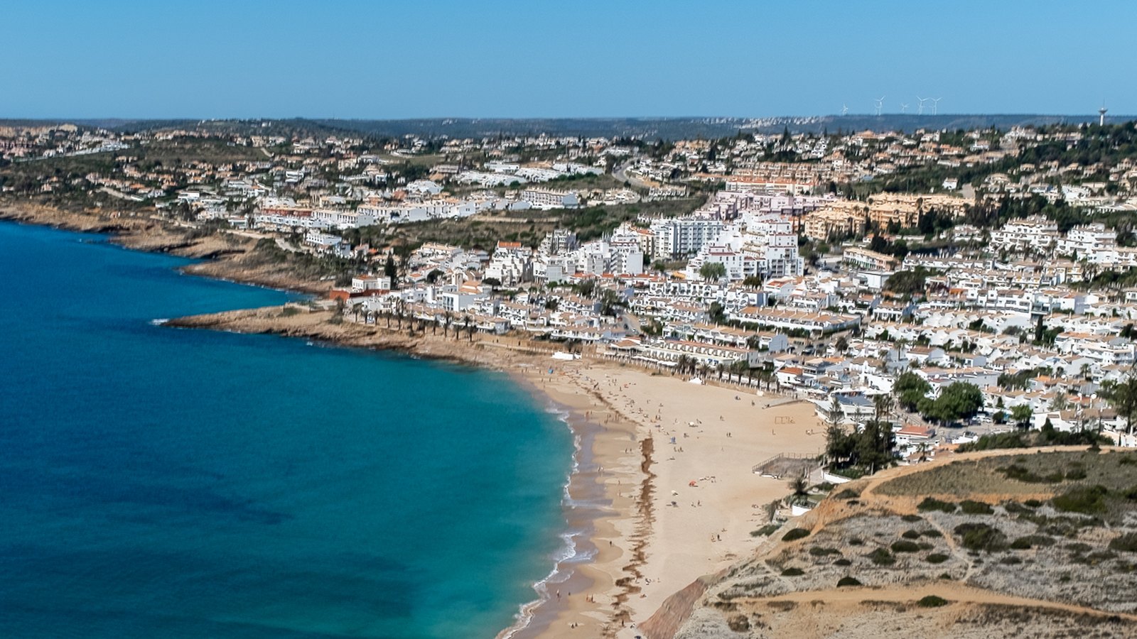 Aerial view of Praia da Luz, Portugal, showing the horseshoe bay, sandy beach and low-rise white village west of Lagos