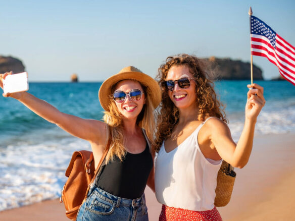 Two American women with a US flag on a beach in Lagos, Algarve, illustrating foreign buyers and Algarve property prices
