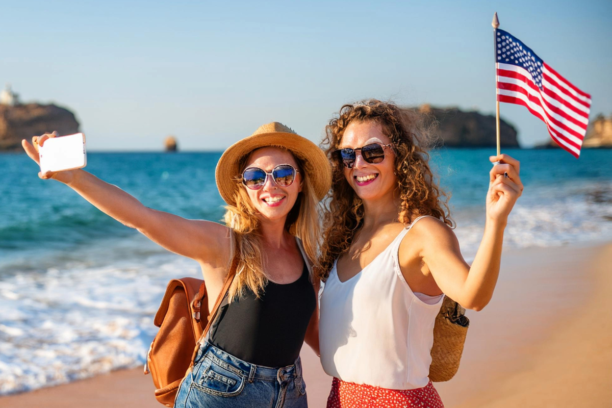 Two American women with a US flag on a beach in Lagos, Algarve, illustrating foreign buyers and Algarve property prices